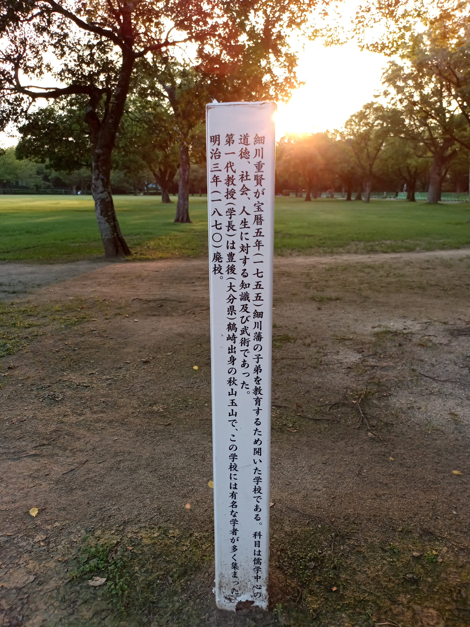 樹木に囲まれた時習館跡の説明板。時習館の創設や教育内容が縦書きで記されている。
